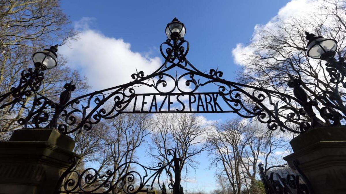 The entrance to Leazes Park which shows a gothic looking gate. There are trees in the background and a blue sky, lending silhouette feel to the whole picture.