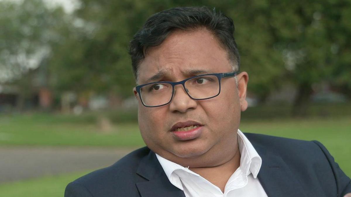 Dr Nish Mathew from the Royal College of Psychiatrists sitting on a bench in the street wearing a white shirt and a black suit jacket looking serious