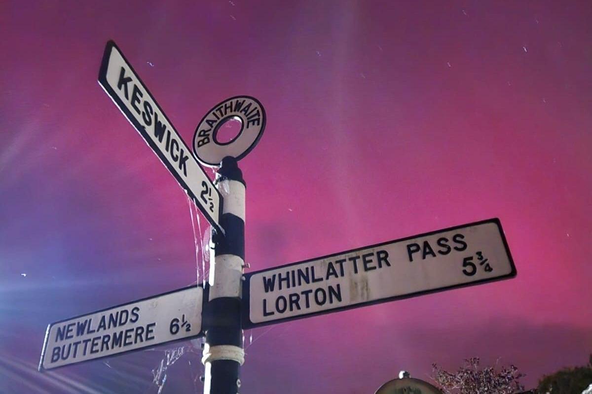 Purple skies behind an old-fashioned, black-and-white signpost pointing to Keswick, Buttermere and Whinlatter Pass.