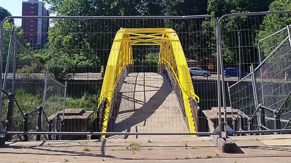 The side of the so-called banana bridge which crosses the Avon New Cut in Bristol. It's a yellow, newly painted bridge, with fences up in front of it before the reopening.