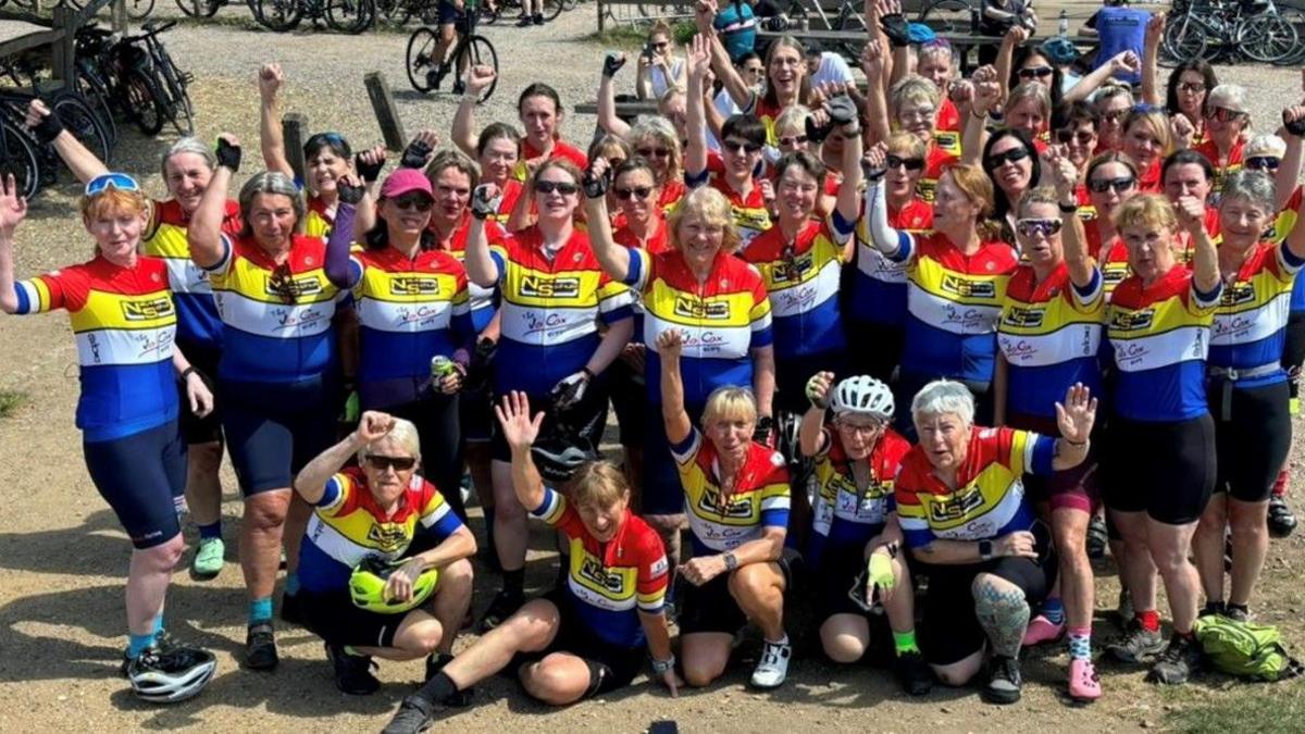 A group of female cyclists celebrate after completing the Jo Cox Way ride last year. They wear cycling outfits of red, yellow, white and blue. Some wear helmets or cycling sunglasses.