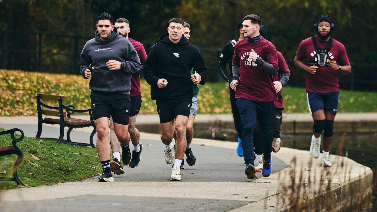 Seven men run around a park - Kieran Conway, in a black hoodie and shorts, leads the way with the others close behind