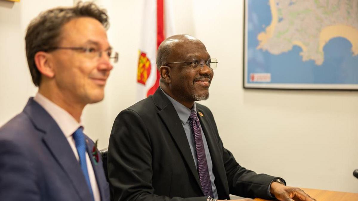 Minister Daryll Matthew pictured with Deputy Kirsten Morel. Minister Matthew is seen wearing a black suit, with a grey shirt and a purple tie. Deputy Morel was seen wearing a navy blue suit, a pink shirt and a royal blue tie. 