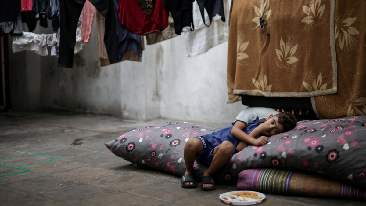 A displaced boy rests in a school in Beirut which provides temporary shelter to the families. A plate of food sits at his feet as he leans to one side resting his head on a pillow