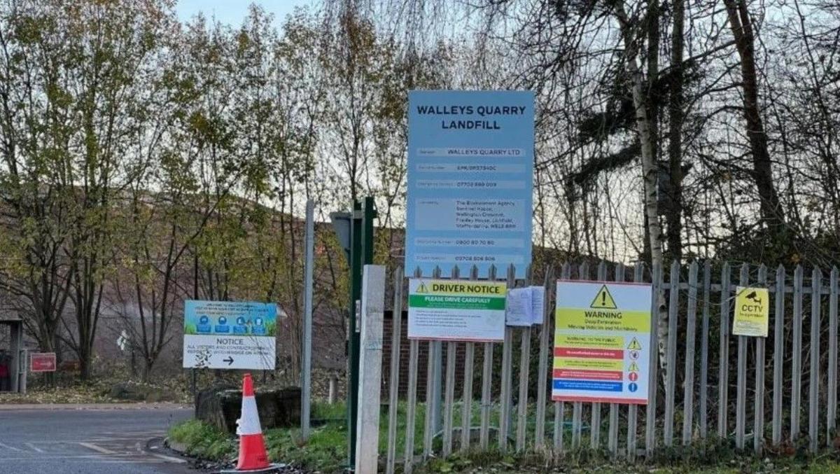 The entrance to Walleys Quarry landfill, with yellow warning signage and fencing in the foreground.