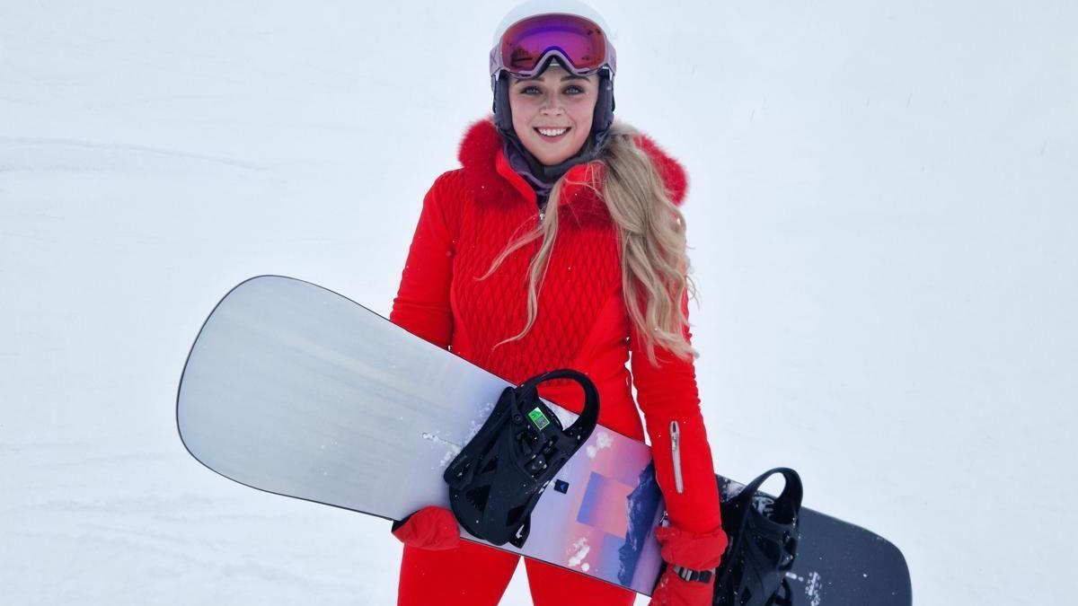 Stephanie Hill on a slope holding a snowboard and wearing a red outfit.