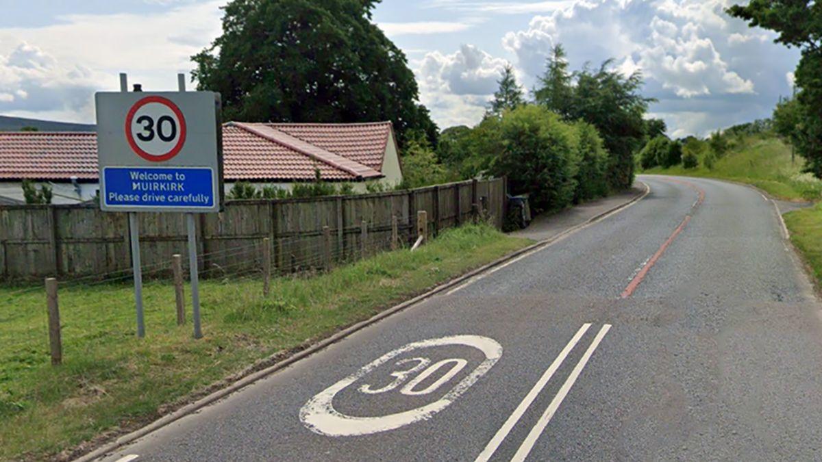 A road between fields with green grass with a 30mph road sign