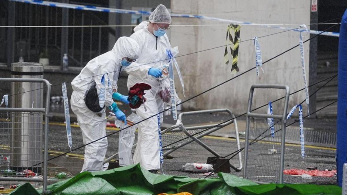 Forensic officers are at the scene in Water Street near the Liver Building in Liverpool. They are wearing while coveralls, face masks and hair coverings and are looking at the ground.