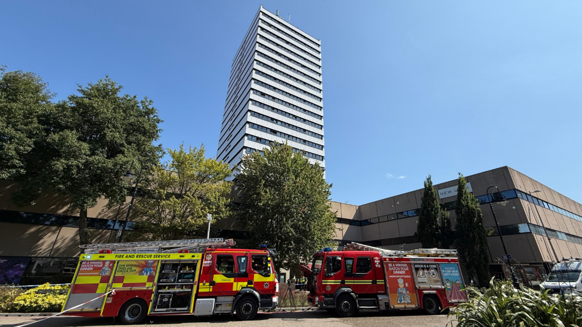 Two fire trucks parked in front of a tower block with lower-rise buildings to the side.