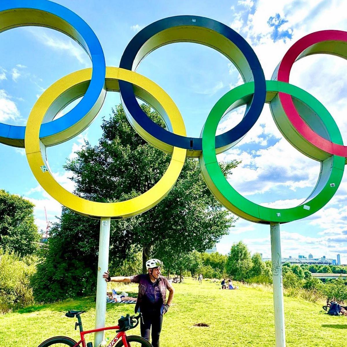 Mr Georgiou with his bike standing in front of an Olympic rings monument