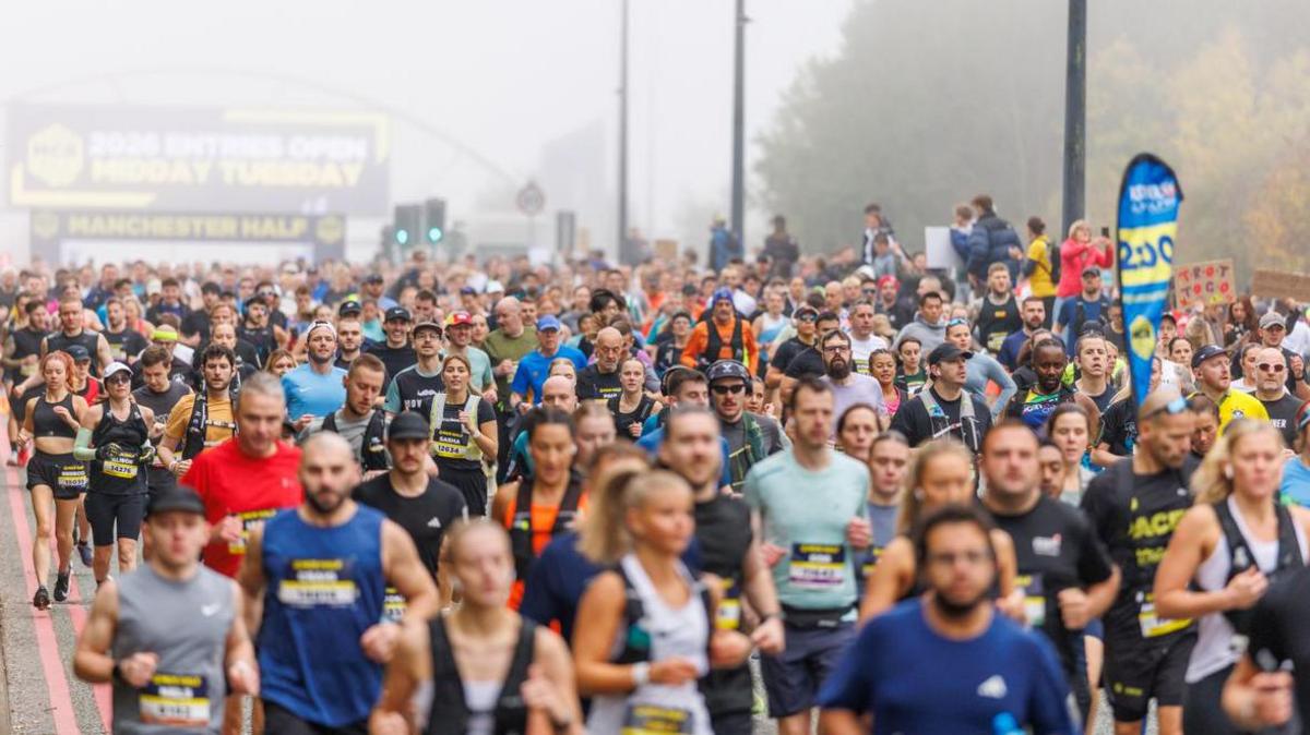 Hundreds of runners set off en masse at the starting point in the fog. Trees line the road to the side.