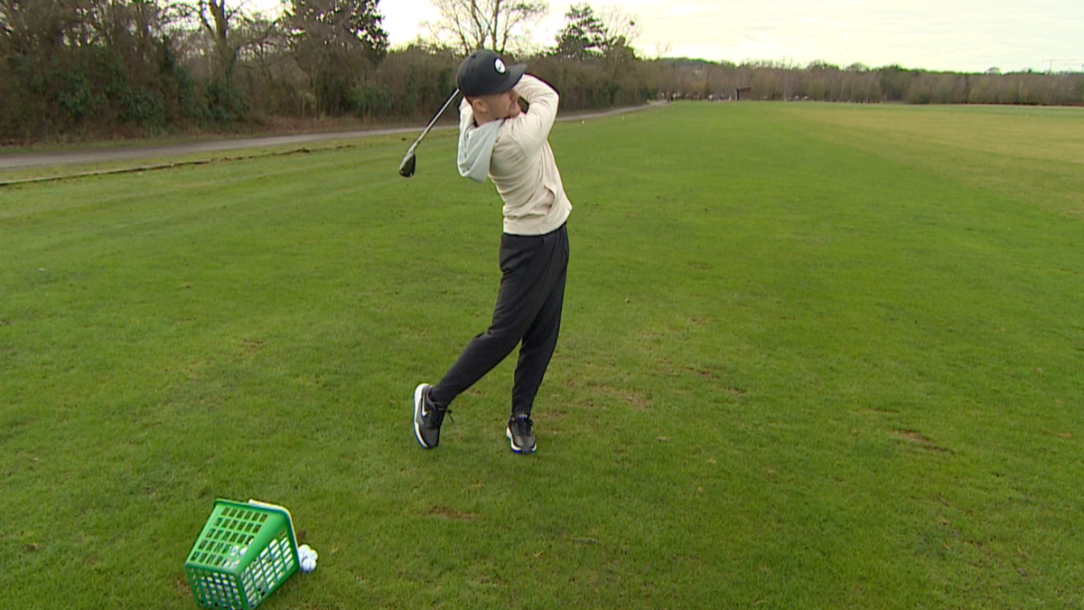Ben Knight, wearing a baseball cap, hits the ball off the tee 