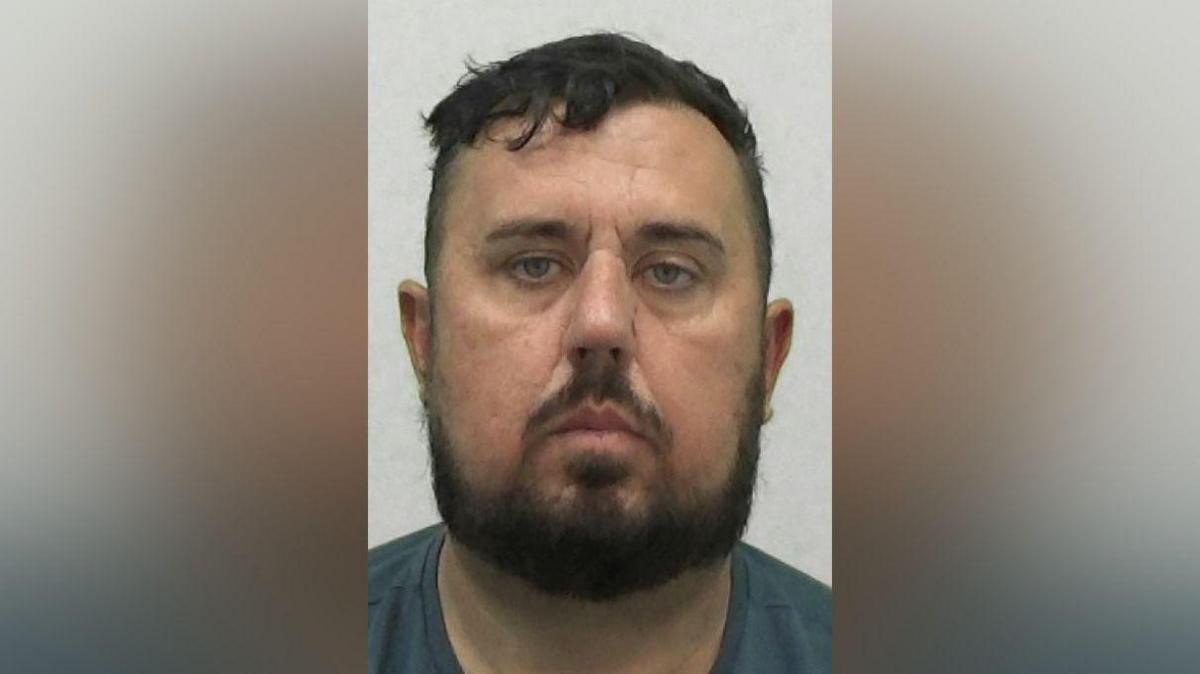 Mugshot of Mark Twizell. He has a short black hair and beard and a long round face.