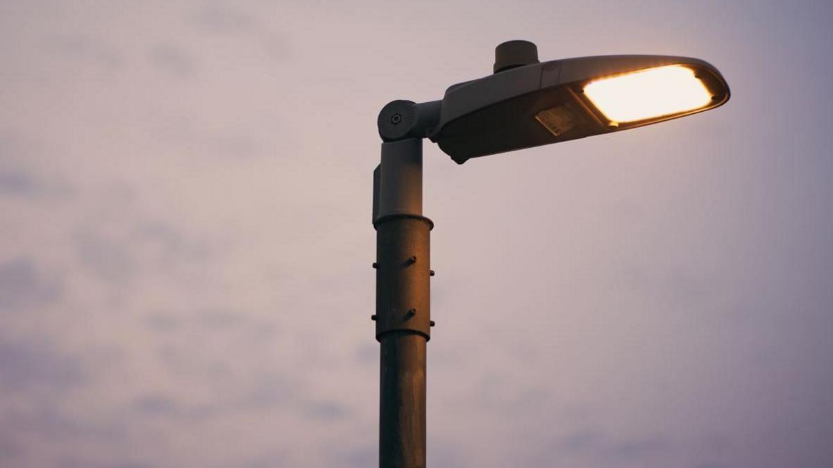 Streetlight lit up. There are white clouds in the background. 