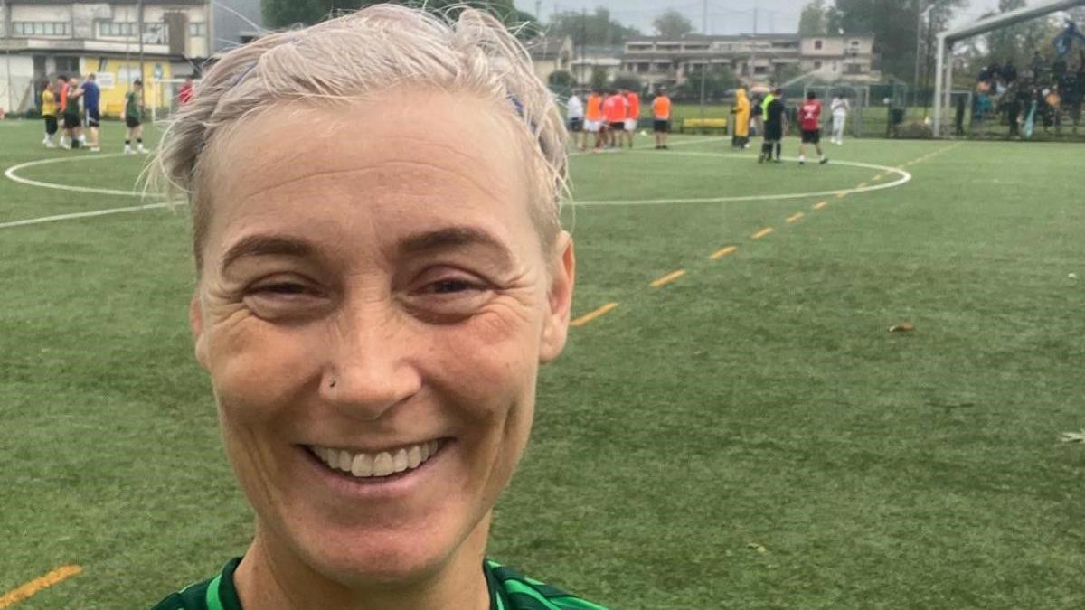 Women looking directly at the camera with light, short blonde hair with a green football field behind her.