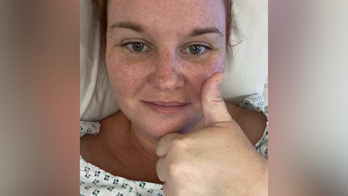 Hayley Combe with her thumb up sat in a hospital bed