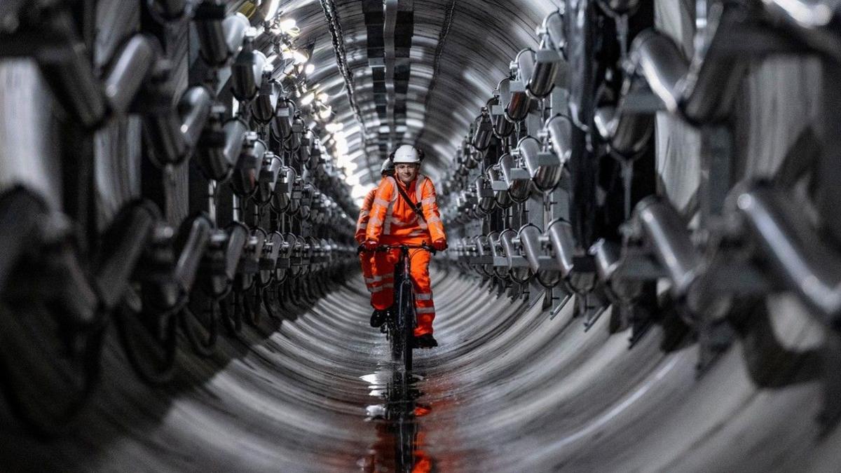 An engineer in a high-viz jacket cycles down a Power Tunnel under London.