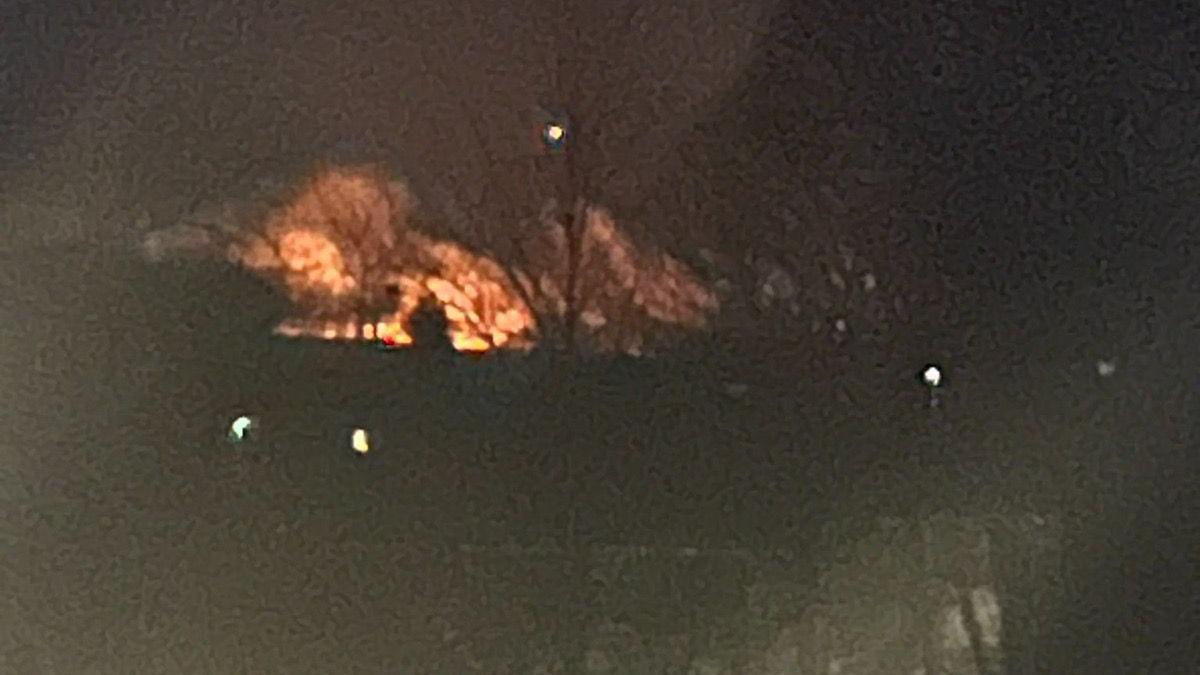 Flames from a fire on Rosenannon Downs head towards the night's sky. The foreground is dark but a set of buildings and trees can be made out.