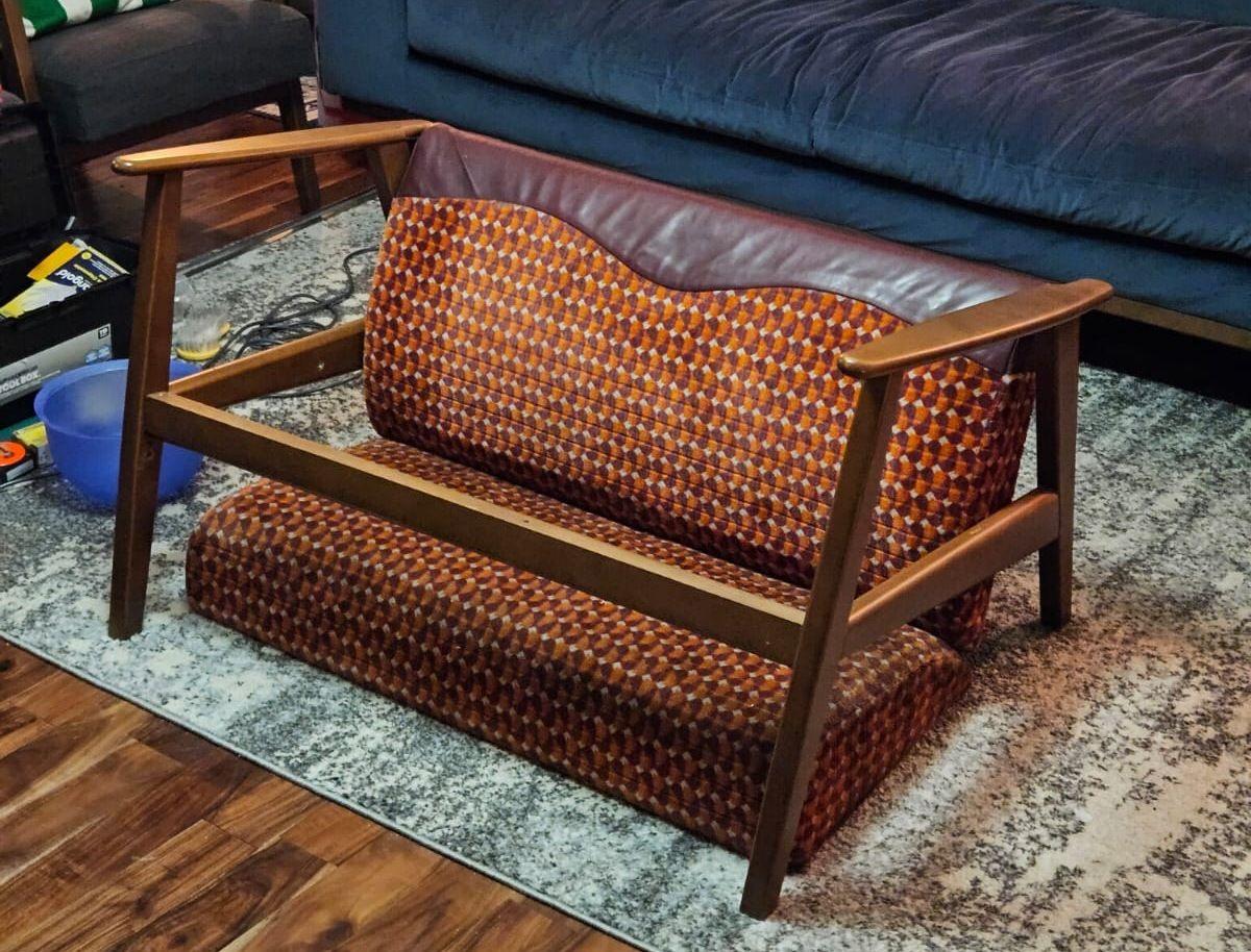 A bright orange and red subway seat converted into a couch with wooden armrests and legs in a living room.