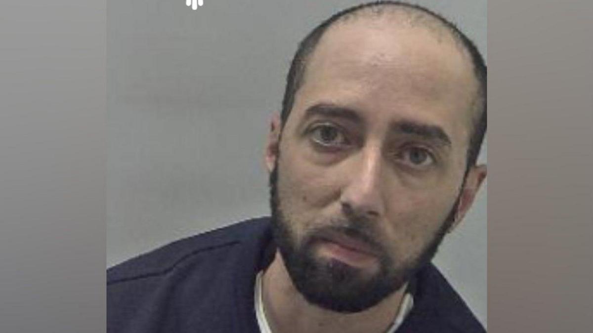 A mugshot of a man, Ulfraz Khan, who has very short black hair and black facial hair.