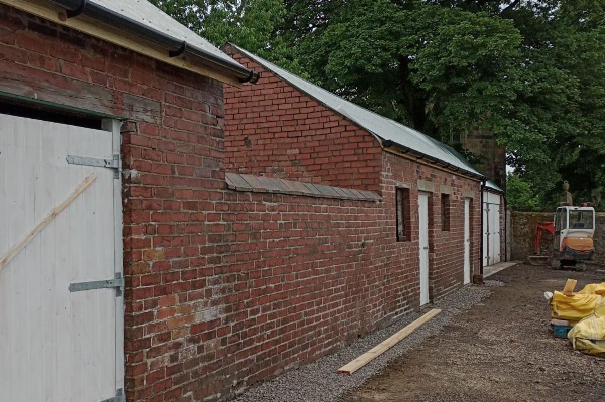 A new roof and gutter are installed on the red brick building - fresh wooden doors are painted white. There is visible work ongoing - a digger in the distace.