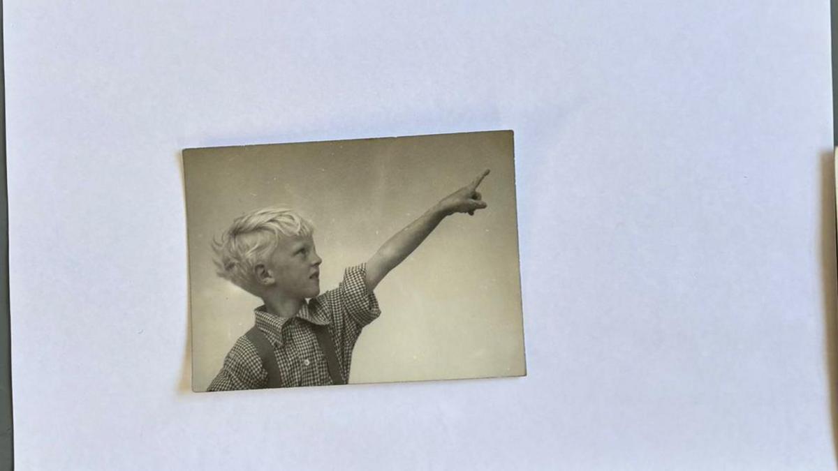 A black and white photograph of a boy with blond hair pointing into the sky.