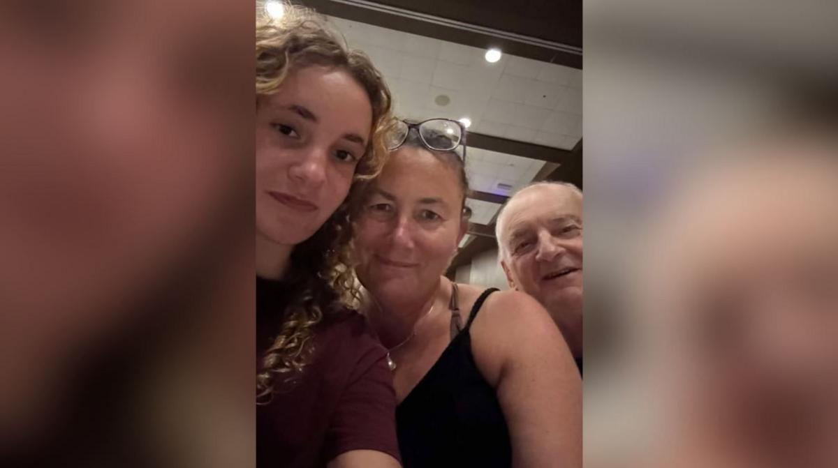 A young woman smiles next to a woman and a man. They all look at the camera.