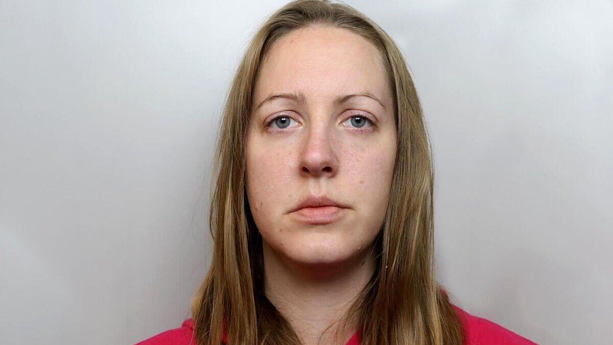 Mugshot of Lucy Letby wearing a red hoody. she has blonde hair and thin eyebrows. 