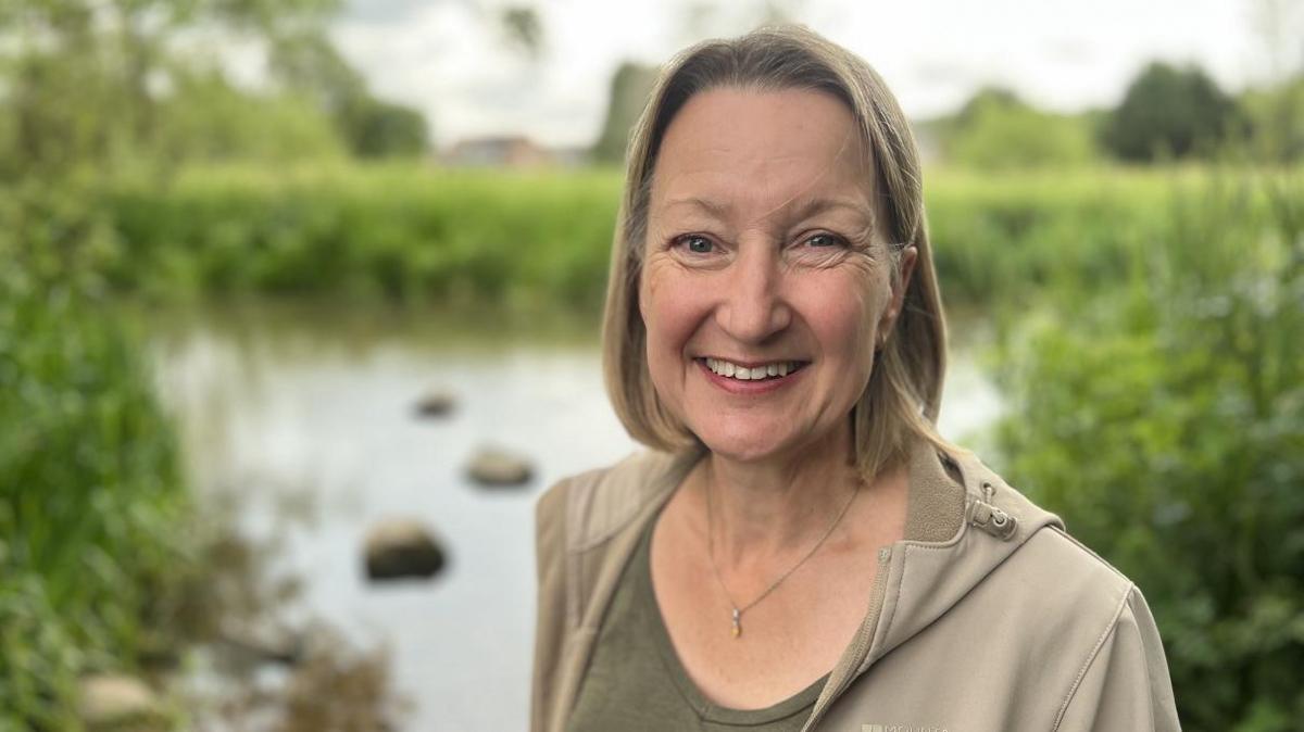 Charlotte Hitchmough smiling at the camera while standing on the banks of the River Kennet