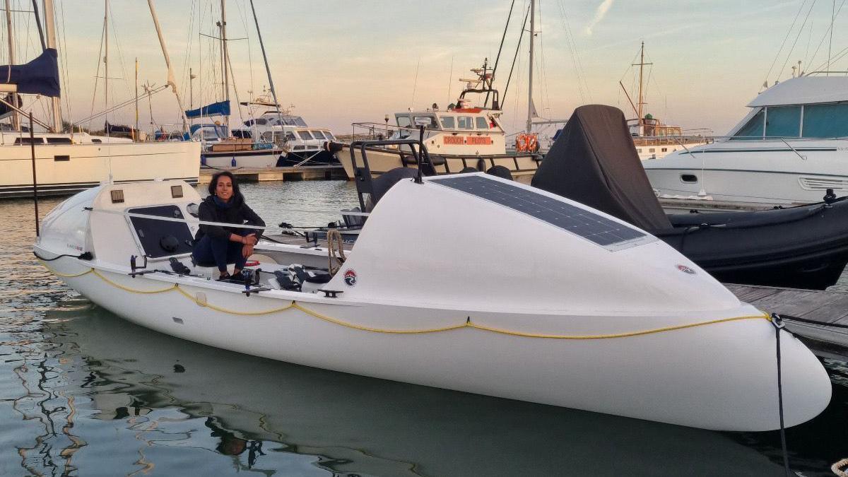 Ananya and her rowing boat are positioned in a marina. Her 'R25' rowing boat is surrounded by larger boats with sails, while hers is sail-less.