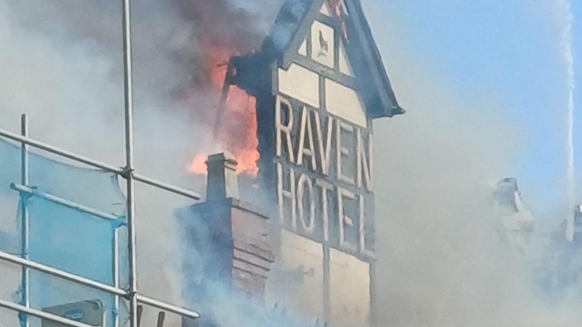 A black and white sign of the Raven Hotel surrounded by smoke and flames.