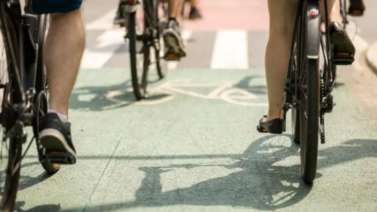People are riding bikes in a cycle lane. There is green painted tarmac with a white image of a bicycle.
