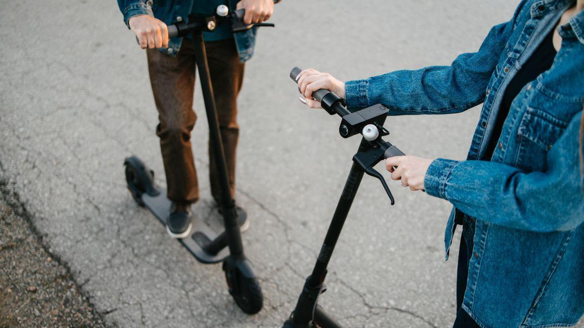 Two people standing on e-scooters wearing jeans and blue denim jackets.