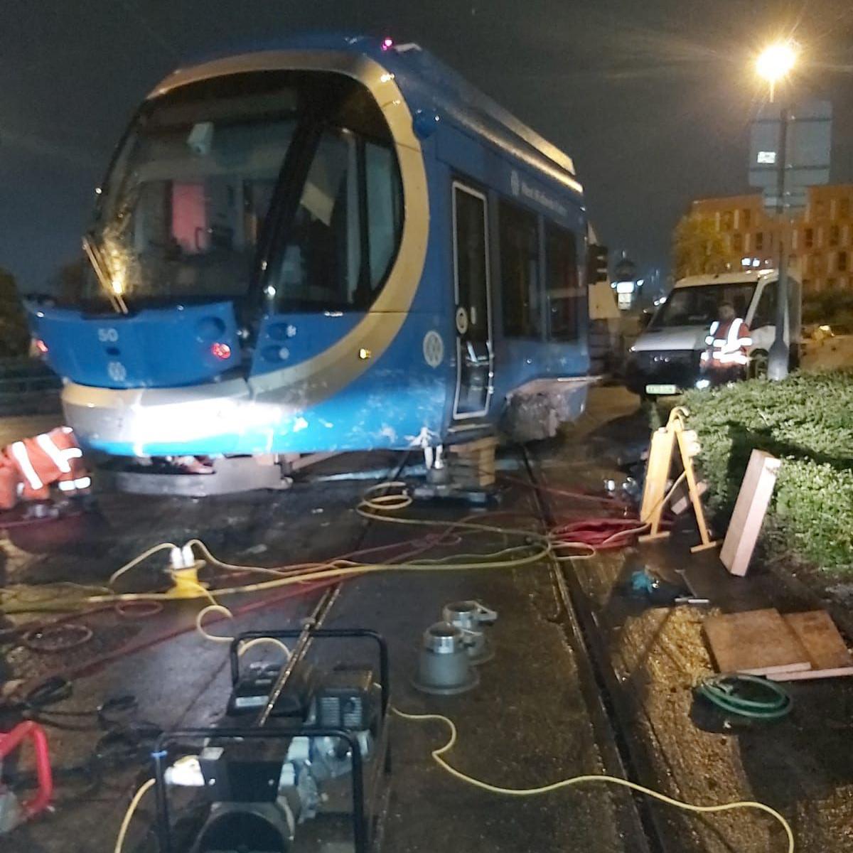 the front of the blue tram with the bumper smashed. Yellow wires and what appears to be a generator are on the floor in front of it