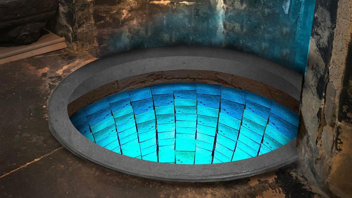 A well set into stone in a cathedral - its walls are lined with turquoise blue mosaic tiles and it is lit in soft blue light.