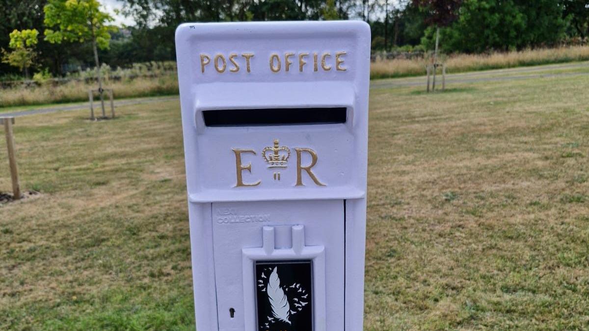 A white post box with the traditional markings including the Royal Cipher of Elizabeth II