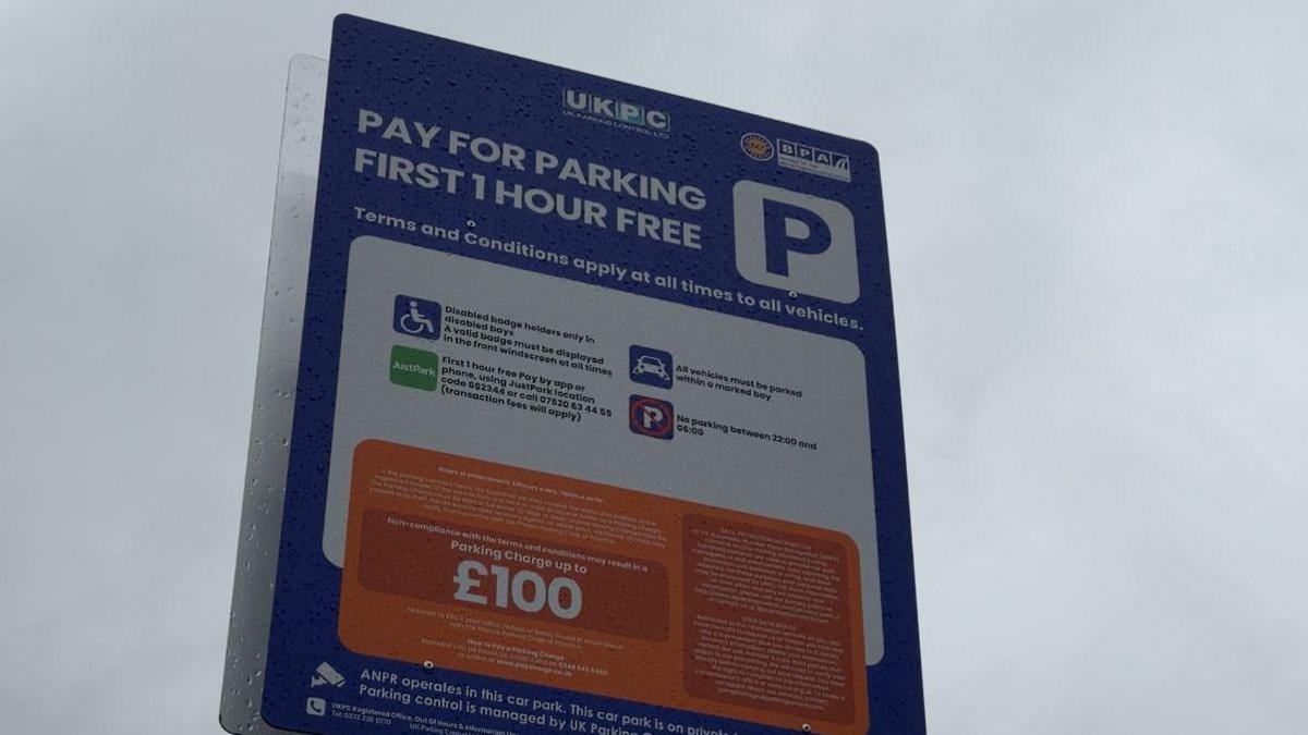 A large red white and orange parking sign with lots of small print, but the fine amount in large bold writing