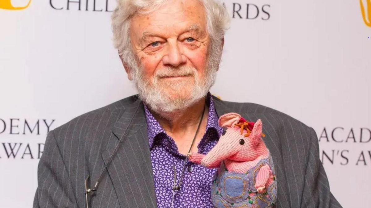 Close up shot of Peter Firmin in 2014 in grey striped jacket and floral mauve shirt with white beard holding a knitted pink Clanger