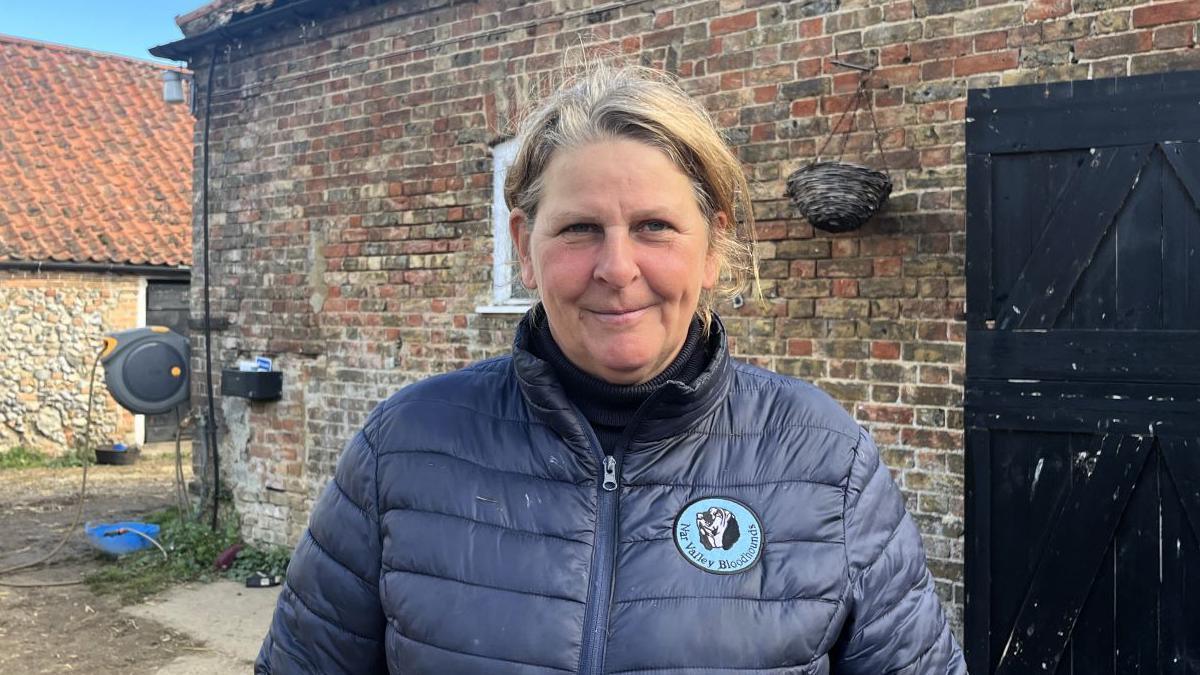 Justine Ward wearing a blue coat and standing in front of what appears to be a barn