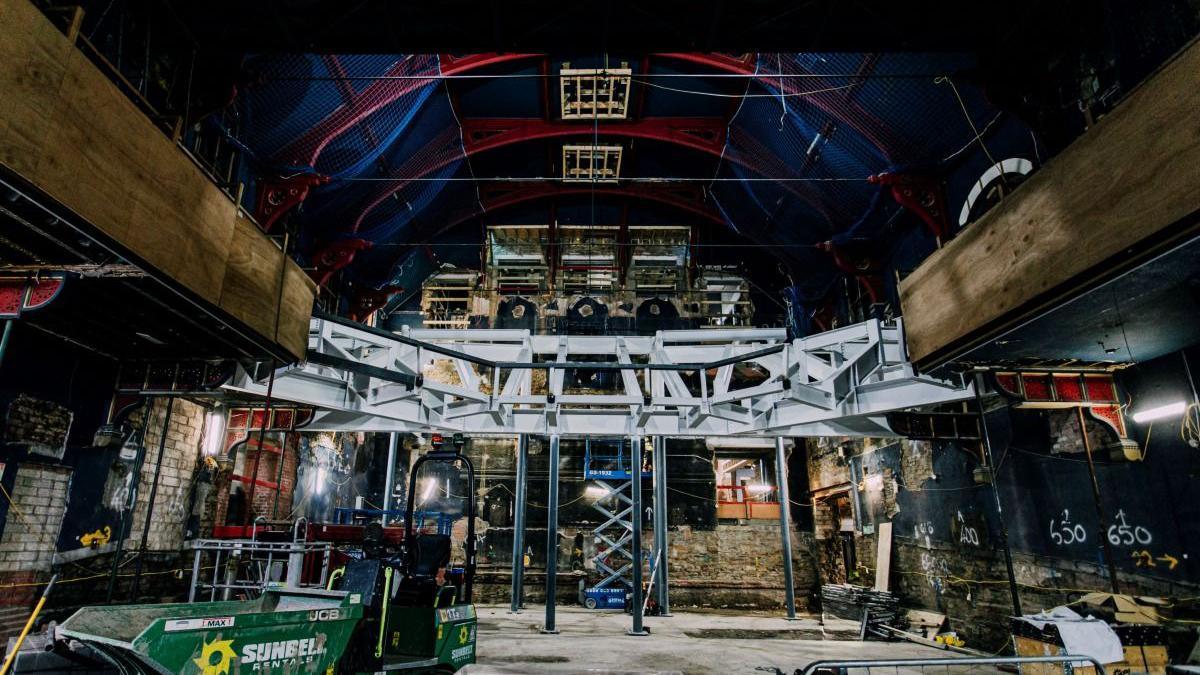 Steel girders elevated over a stage area in a large arched hall