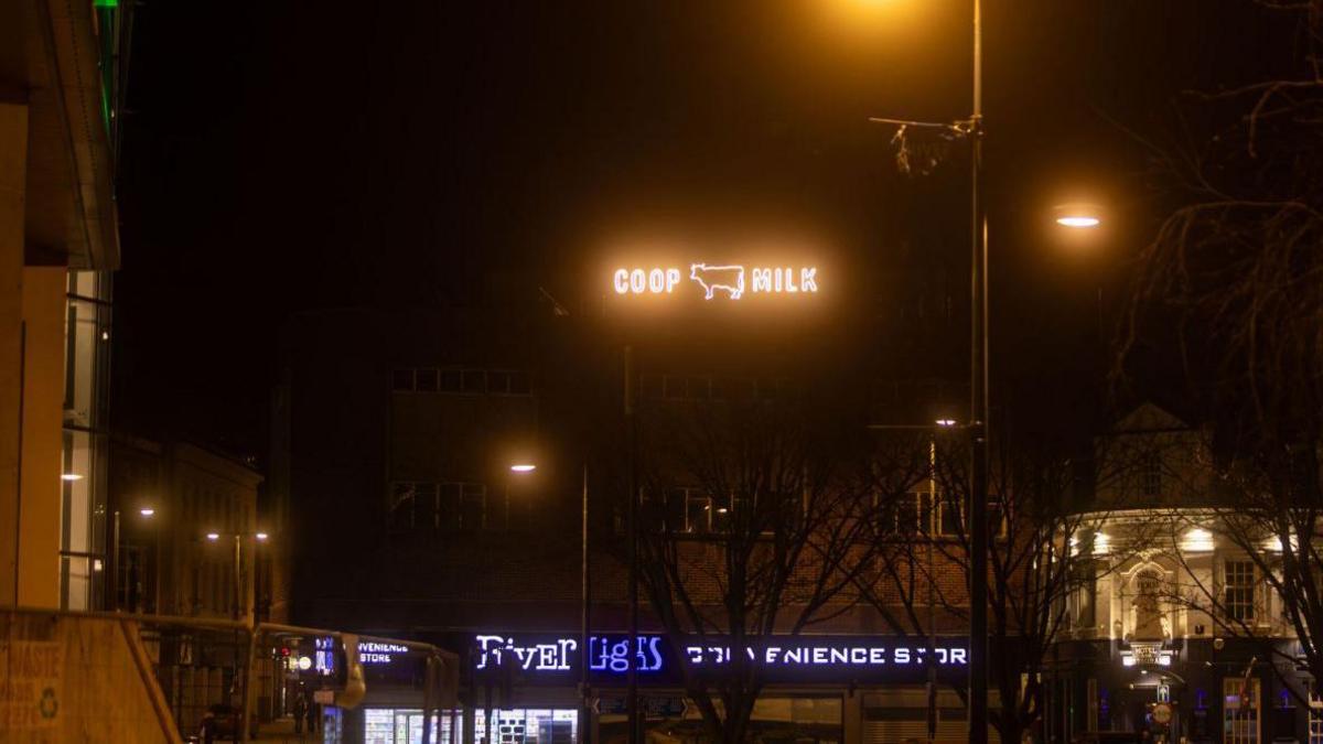 A sign on top of a building in Derby city centre at night which reads COOP MILK