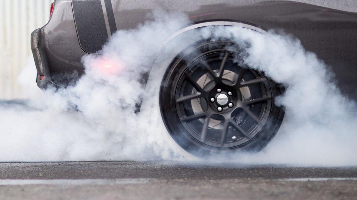 A close-up of a wheel - rubber smoke is coming from the tyre of a black car.