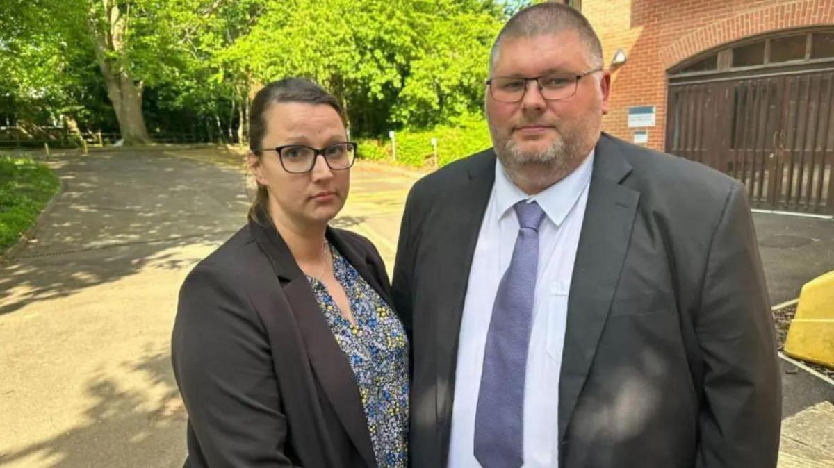 Zoe and Lewis Steeper smartly dressed standing outside coroner's court. They are both looking at the camera, not smiling and there are trees and the red brick building seen behind them.