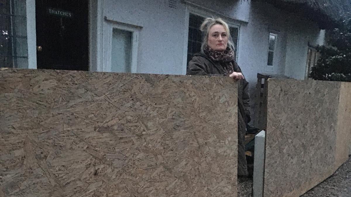 Blonde woman standing next to wooden boards while standing outside her cottage in Essex