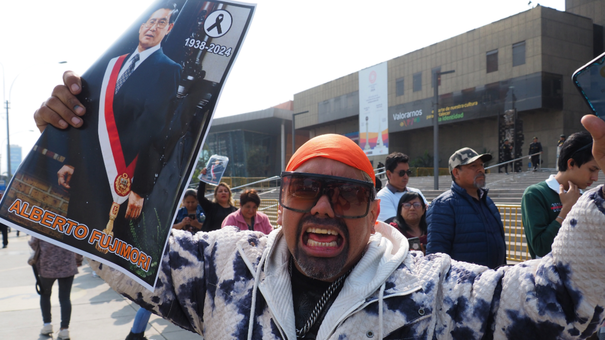 A supporter of Alberto Fujimori wearing an orange headgear, sunglasses and a blue and white patterend jacket expresses his grief while holding an image of the former president.