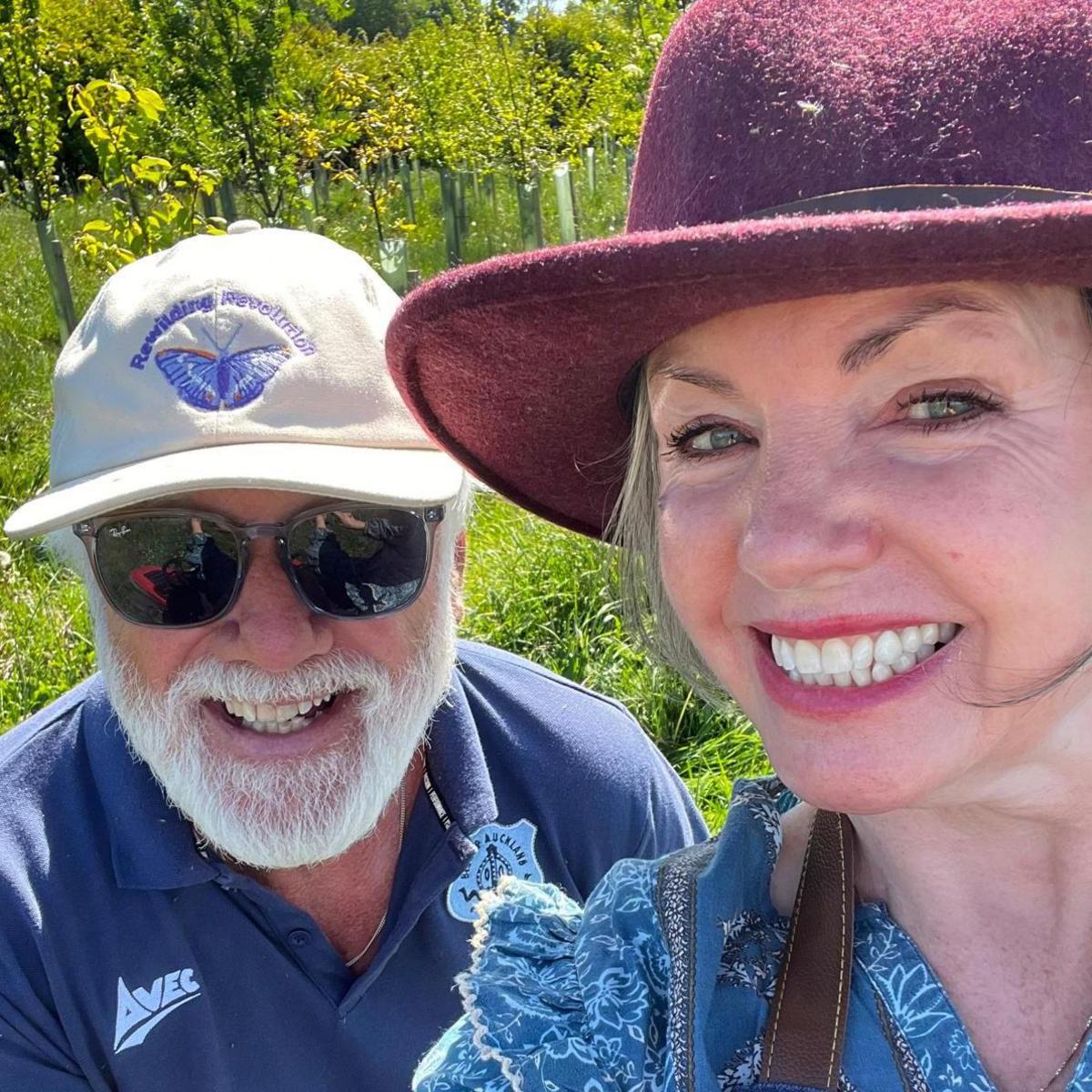 Tracy and Terry smiling in the woodland with rows of new trees behind them.