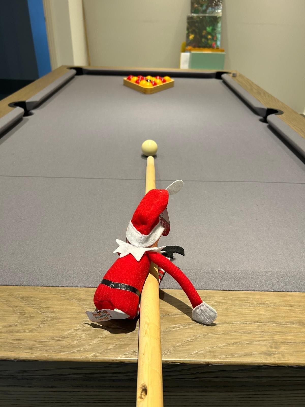 An elf holding a pool cue, as he prepares to strike the cue ball.