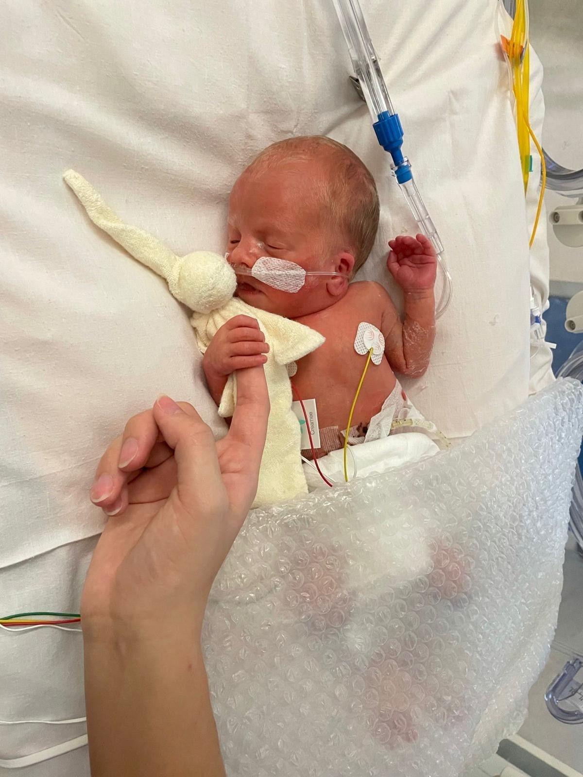 Tiny baby Zachary in a hospital cot hooked up to machines and holding his mum or dad's finger