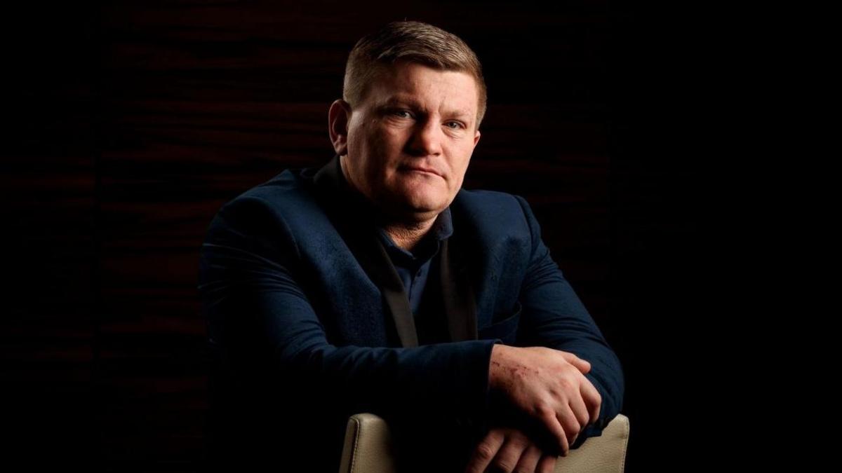 Ricky Hatton is staring straight at the camera in this posed photograph. He is wearing a navy suit and shirt.