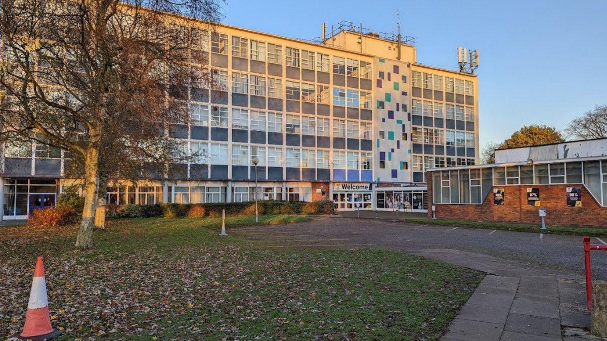 A five-storey building with many windows and a welcome sign outside on the ground floor.